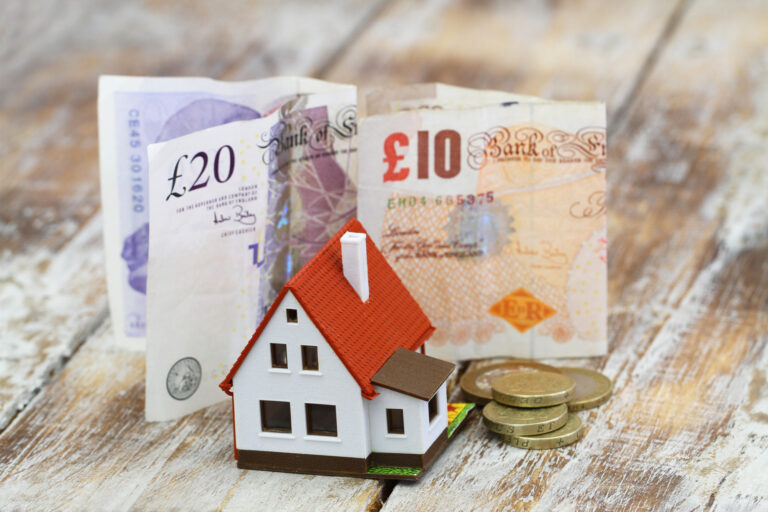 British pound displayed with housing market replica and currency coins in view referencing foreign exchange currency.